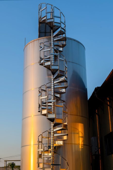 Metal wine storage tanks with spiral staircase to the top in Chateau Vartely at sunset, Orhei, Moldova